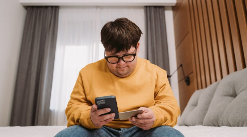 man in yellow sweater holding black smartphone and credit card