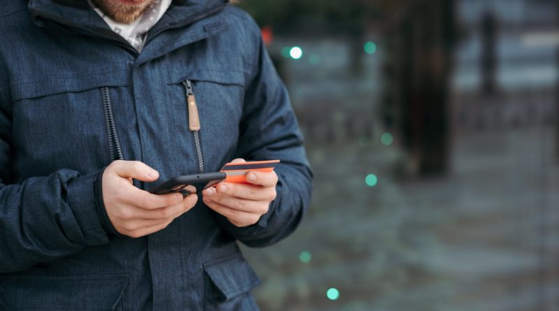 man browsing smartphone and holding credit card on street