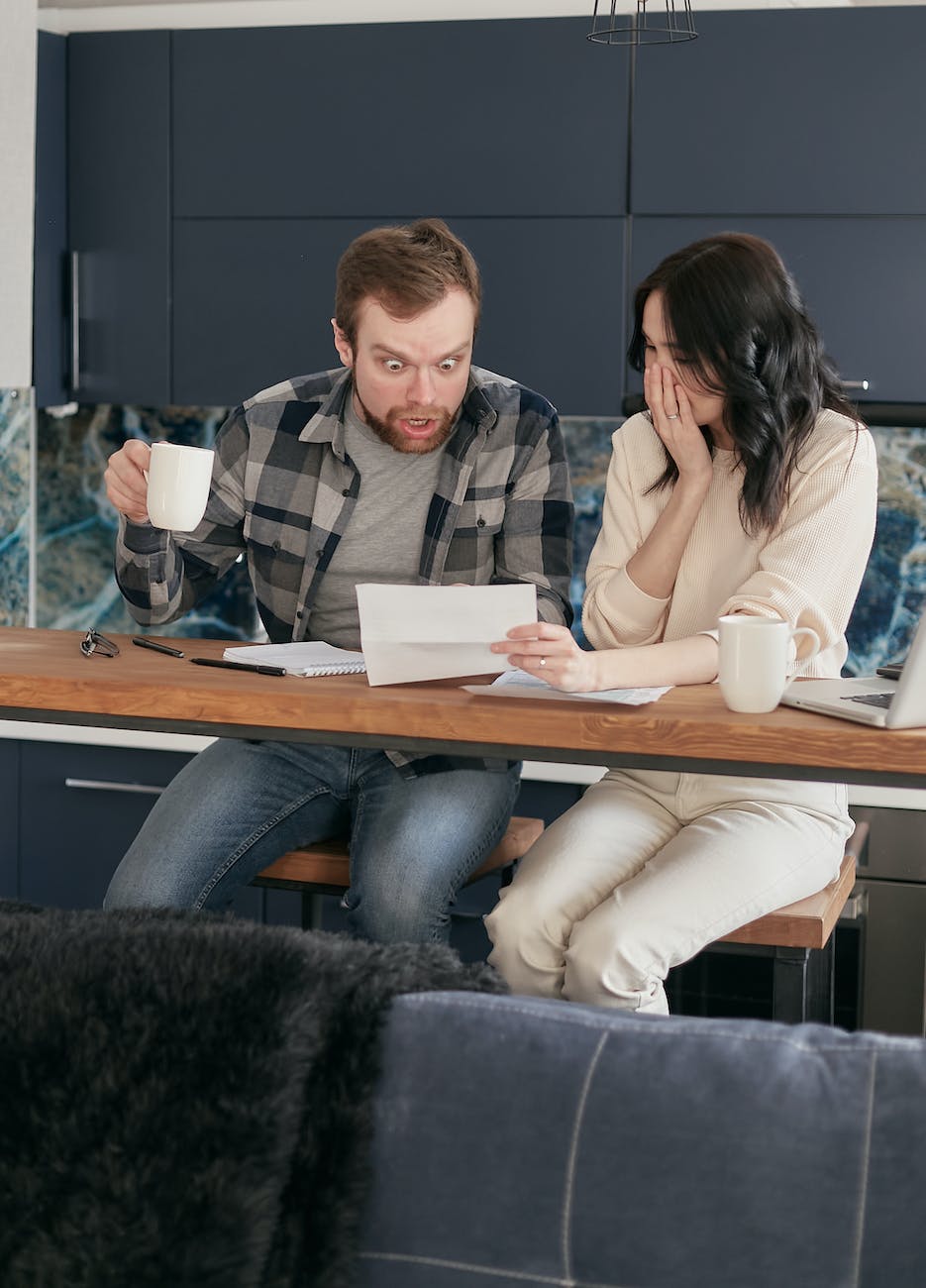 a couple sitting near the wooden table while looking at the document in shocked emotion